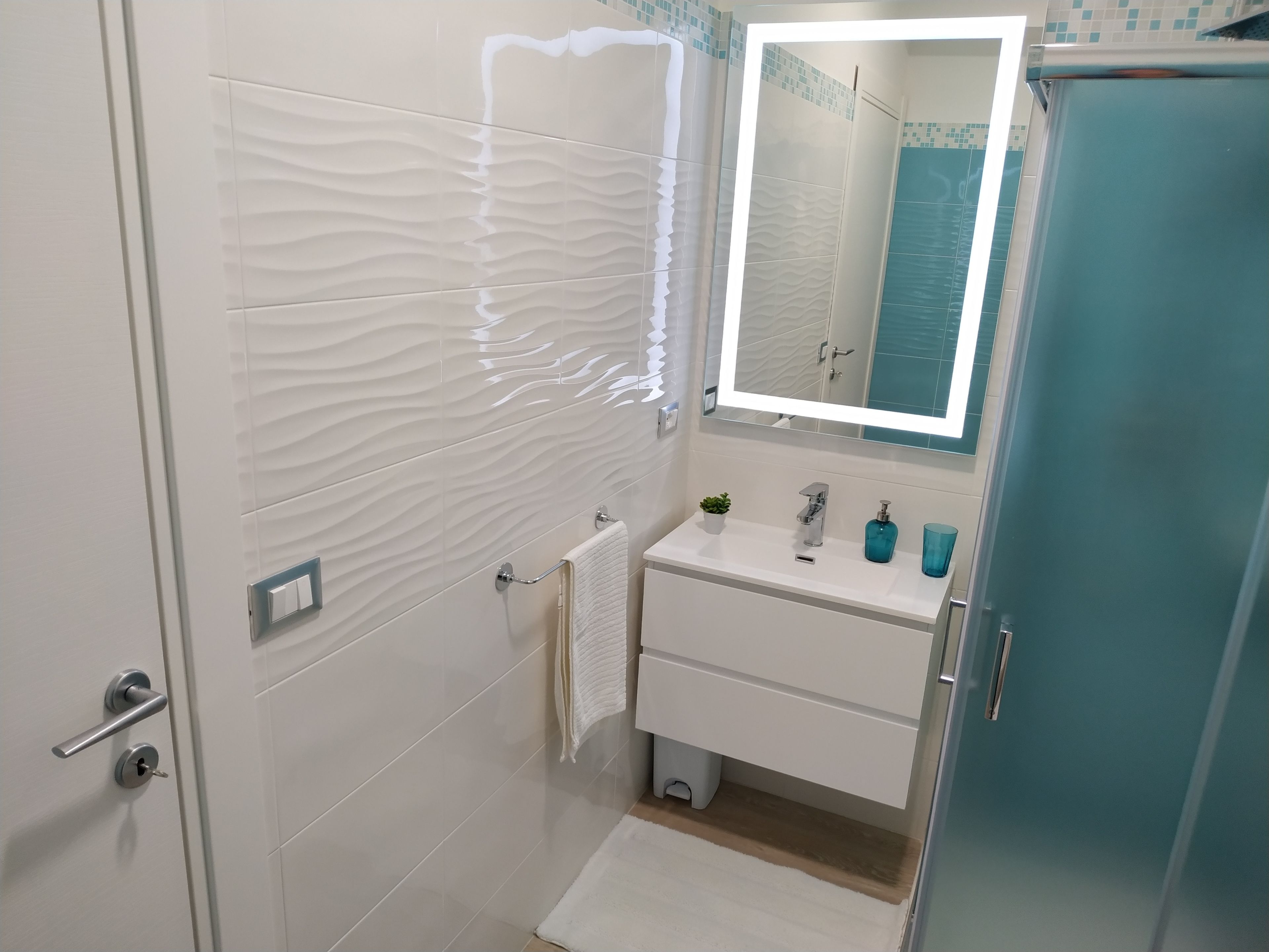 A modern bathroom with a white vanity, a mirror, and a shower area.