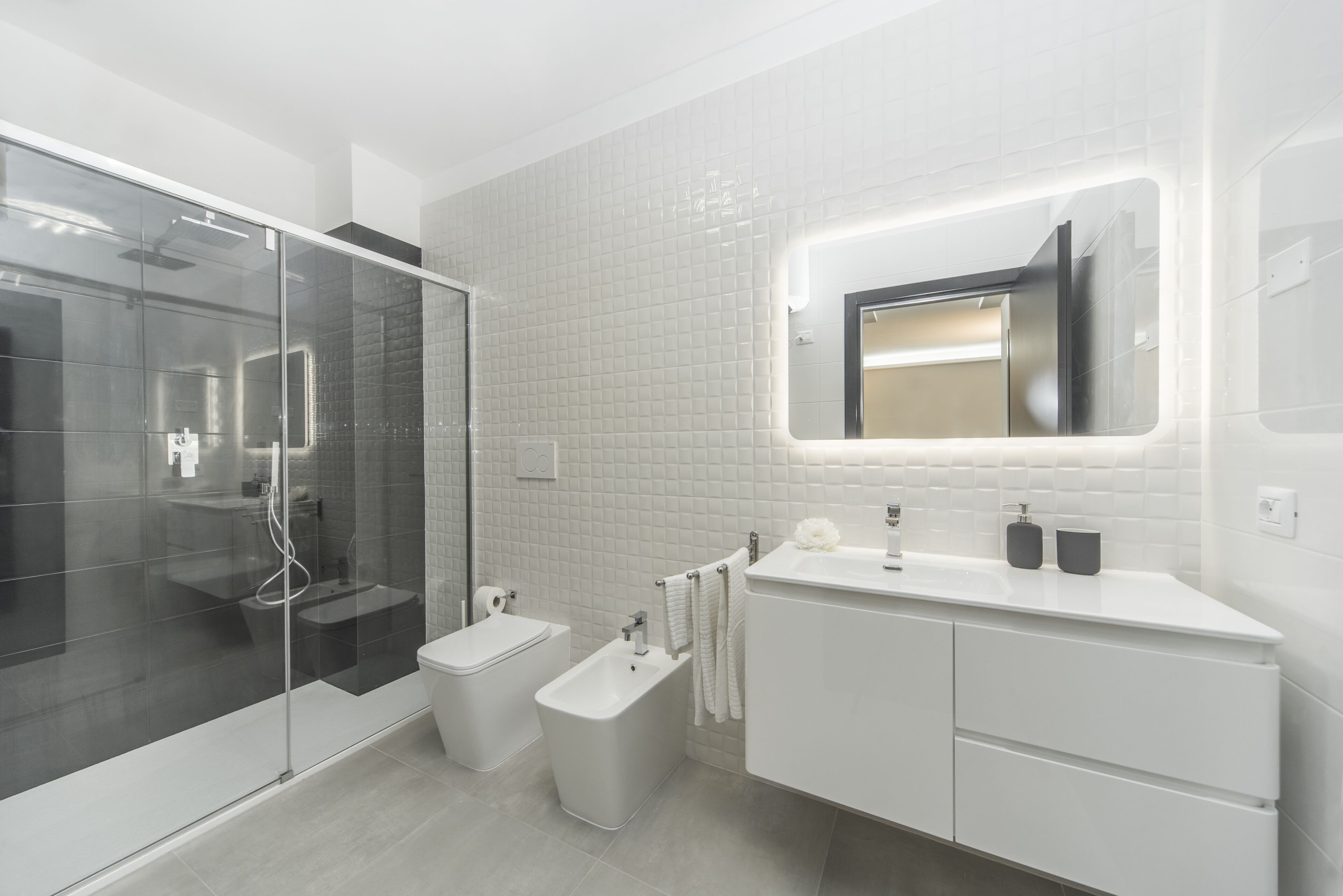 A modern bathroom with a glass shower enclosure, a bidet, a toilet, and a vanity with a mirror.