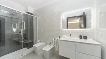 A modern bathroom with a glass shower enclosure, a bidet, a toilet, and a vanity with a mirror.