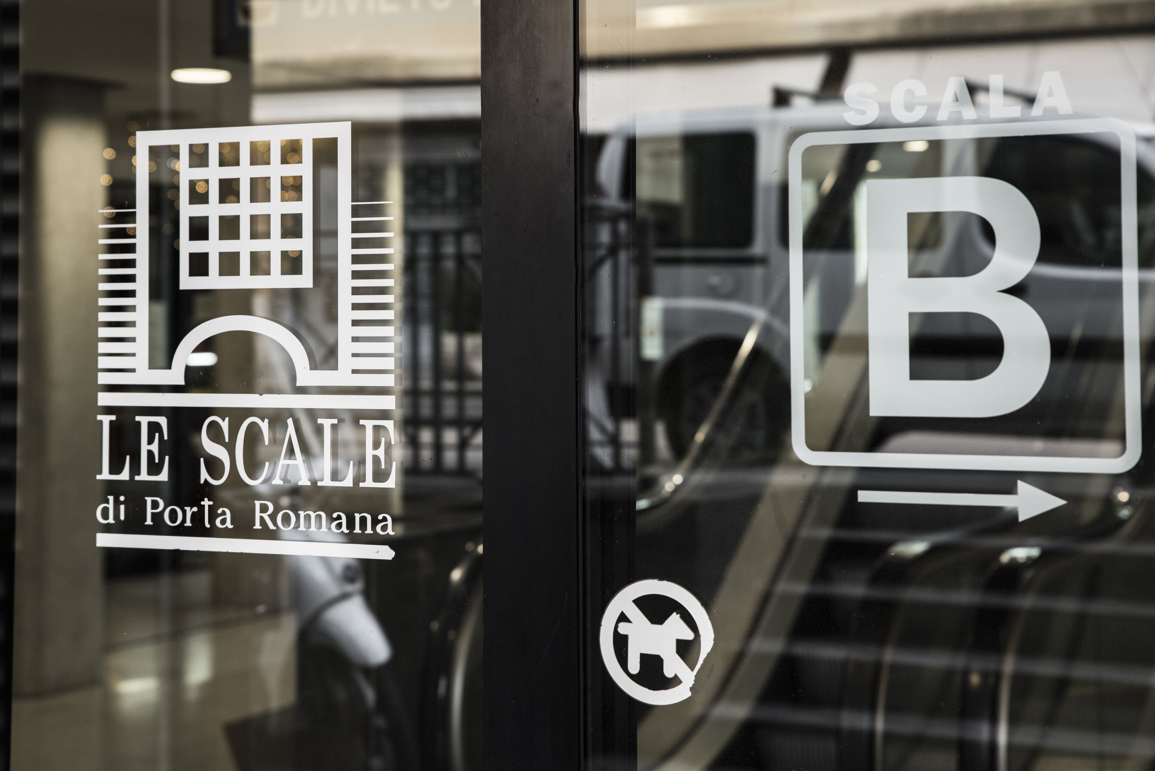 A glass window with the text "LE SCALE di Porta Romana" and a "B" symbol with an arrow.