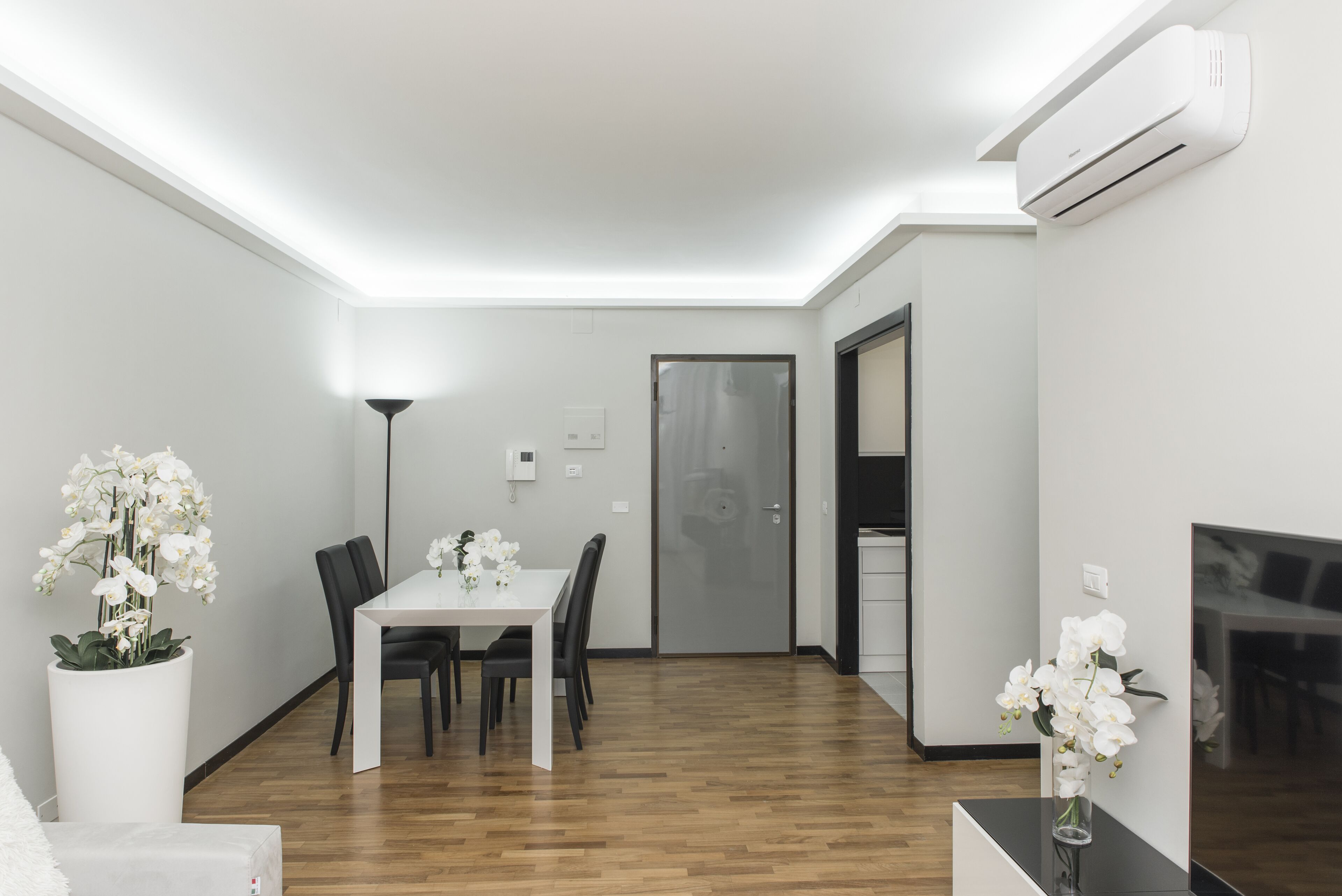 A modern dining area with a white table and chairs, white orchids in vases, and a wooden floor.
