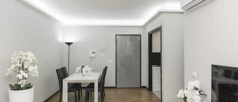 Un comedor moderno con una mesa y sillas blancas, orquídeas blancas en jarrones, y piso de madera.