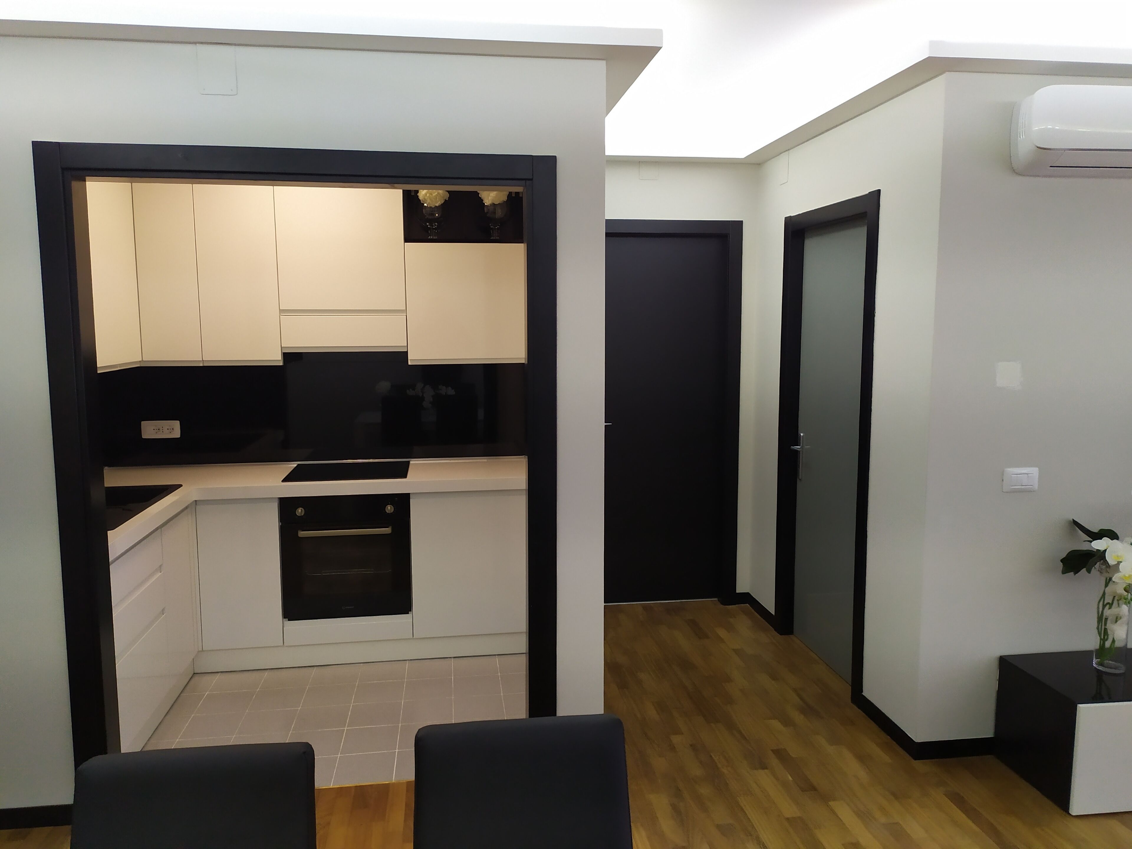 A compact kitchen with white and black cabinetry, a built-in oven, and a black countertop.
