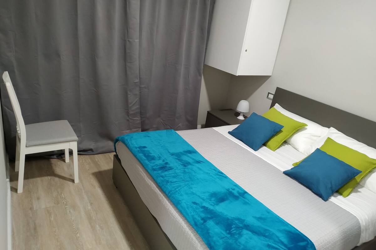 Un dormitorio moderno con una cama, una silla, una mesita de noche y una lámpara.