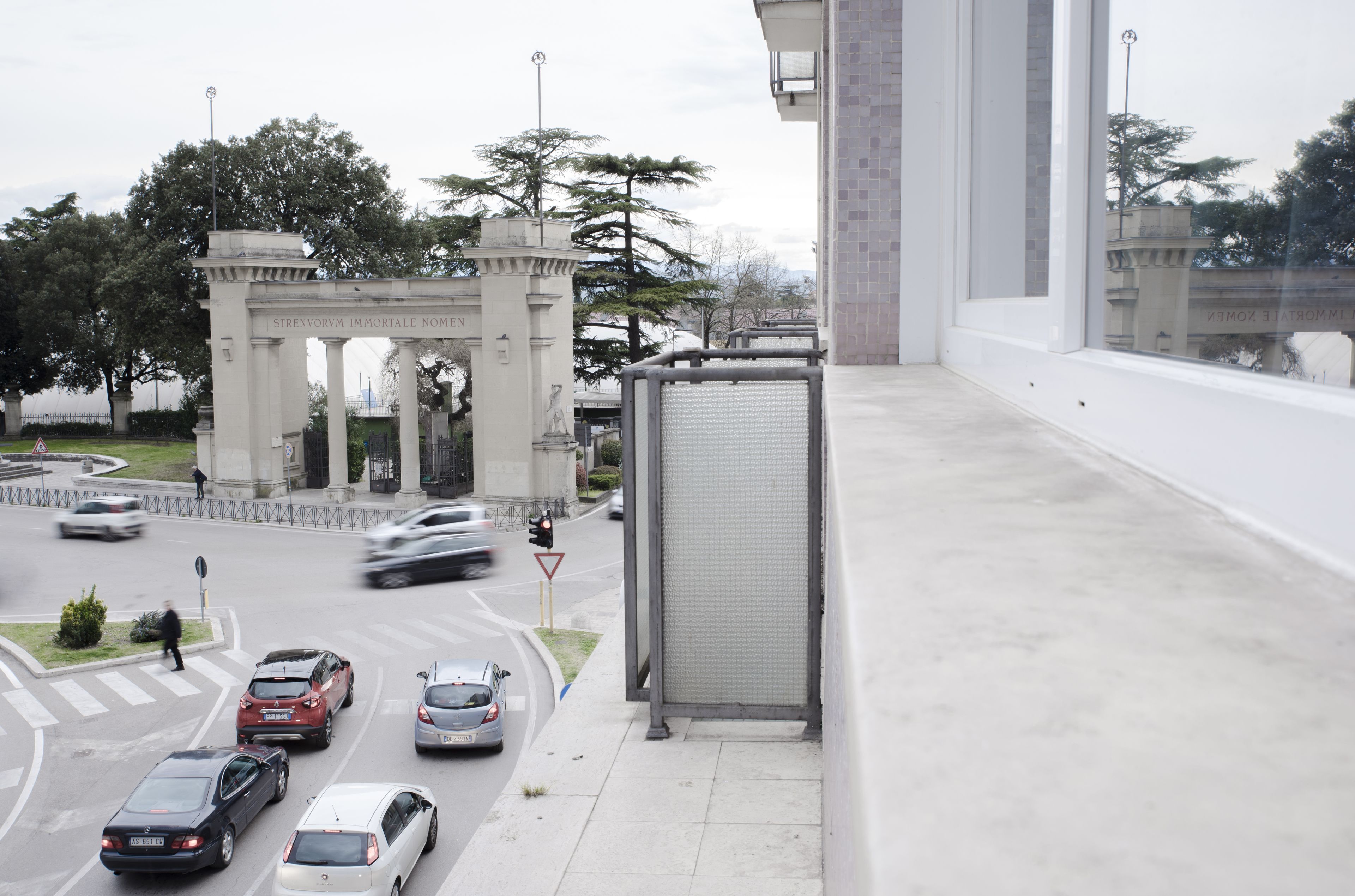 A busy urban street with a prominent archway labeled "STRENVORUM IMMORTALE NOMEN" and a bus stop shelter.