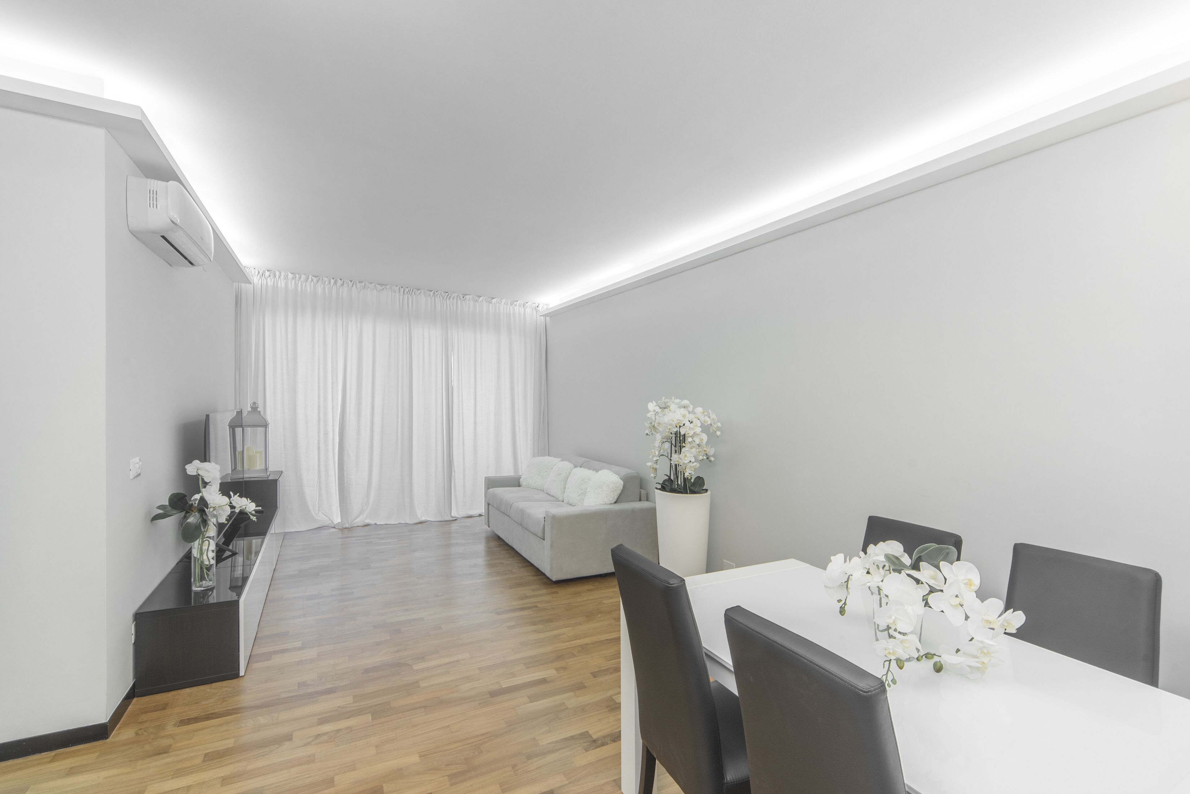 Una sala de estar moderna con comedor, que incluye un sofá, una mesa de comedor con sillas y una planta en maceta con flores blancas.