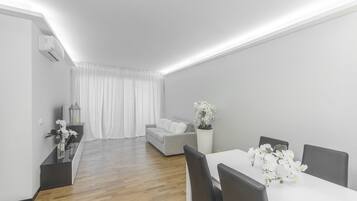 Una sala de estar moderna con comedor, que incluye un sofá, una mesa de comedor con sillas y una planta en maceta con flores blancas.