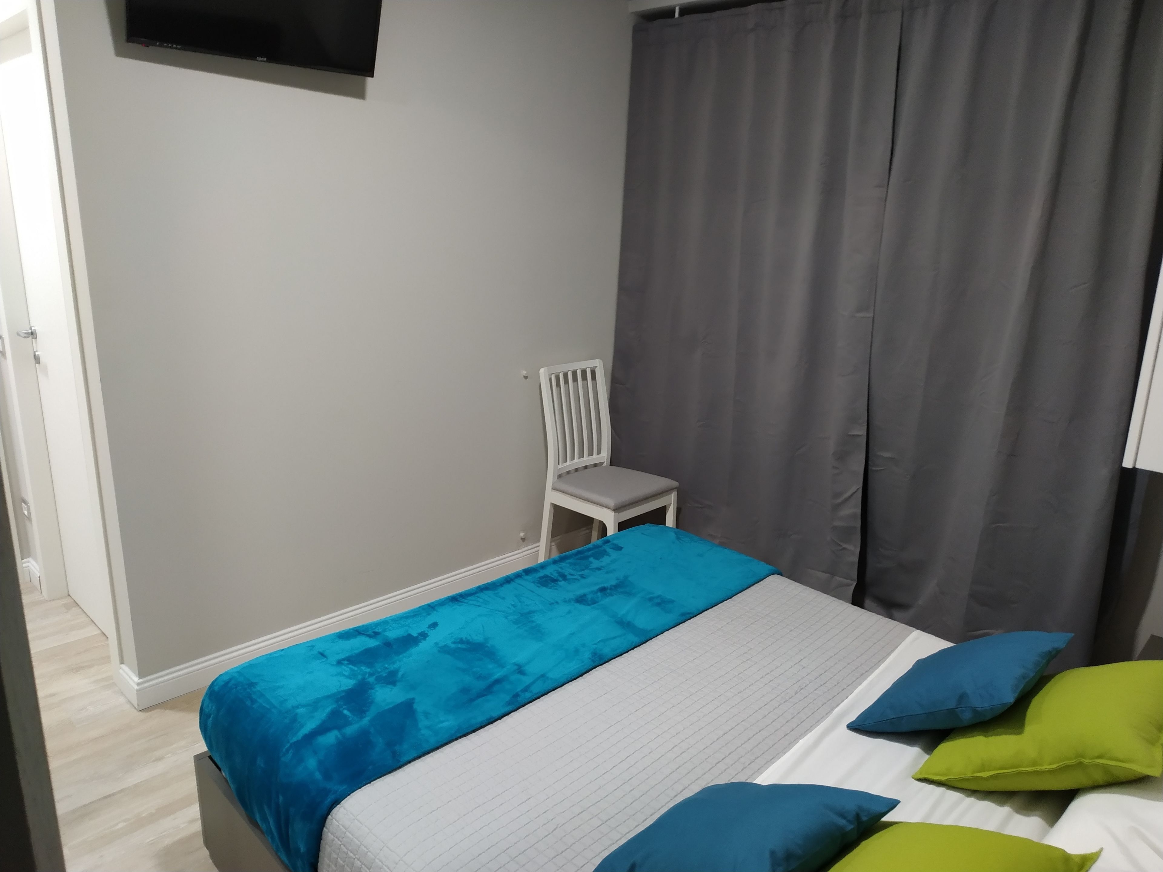 A bedroom with a bed, a chair, a TV, and curtains.