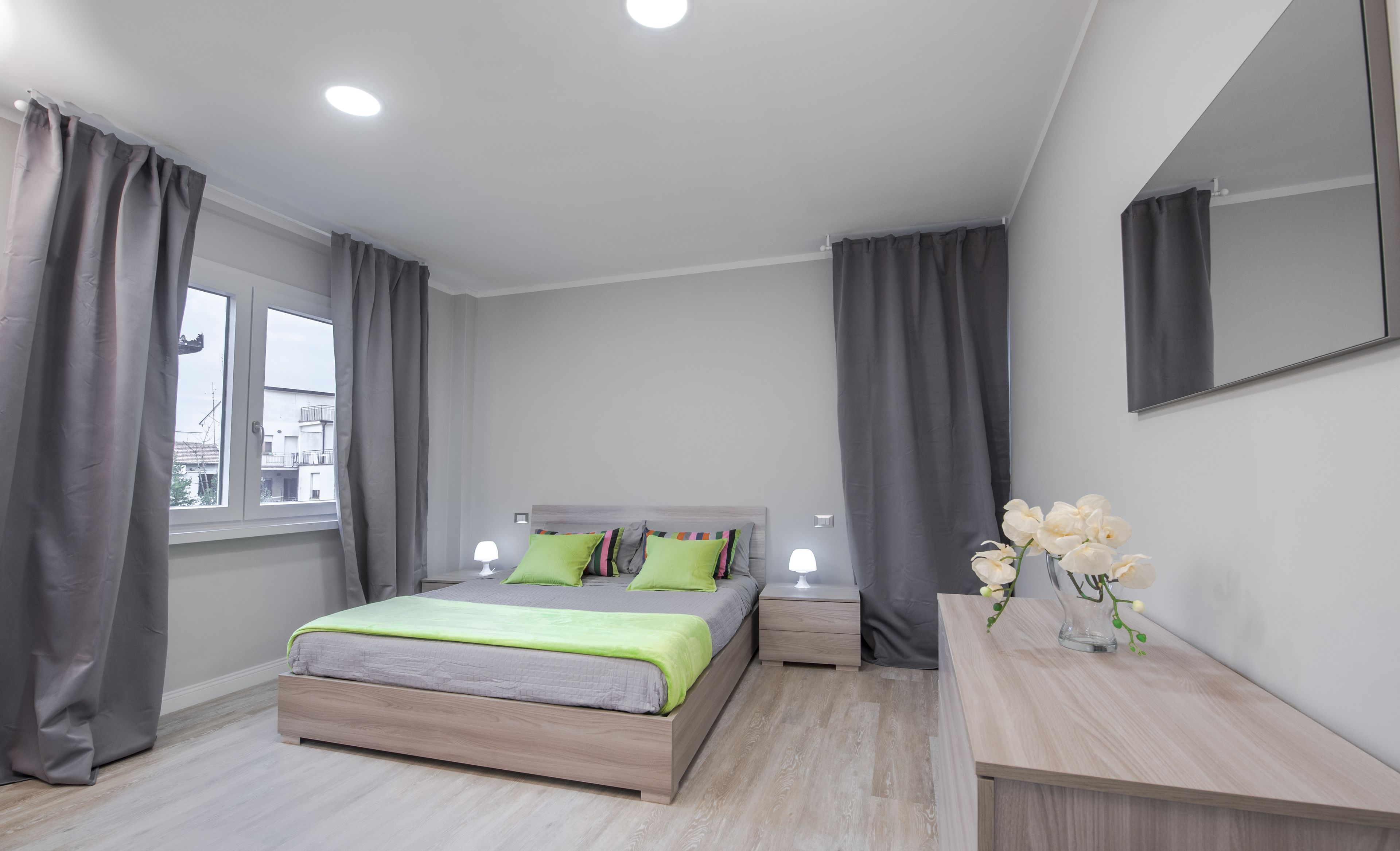 A modern bedroom with a bed, bedside tables, a mirror, and a window with curtains.