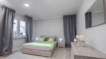 A modern bedroom with a bed, bedside tables, a mirror, and a window with curtains.