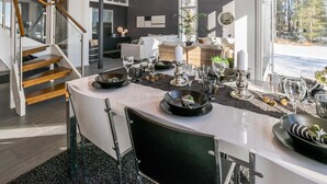 Ein moderner Essbereich mit einem weiß gedeckten Tisch, einer Treppe und Blick ins Freie.