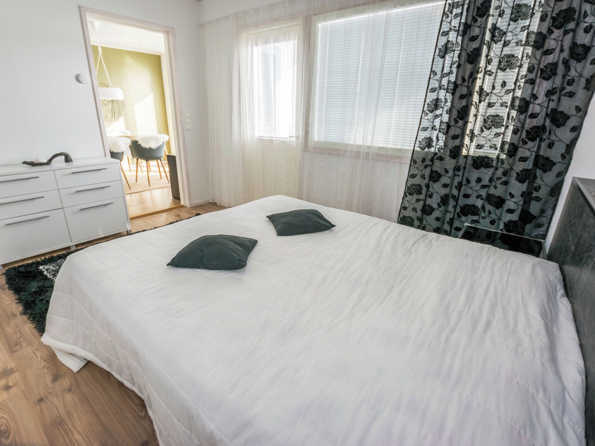 Un dormitorio con cama, dos almohadas, cómoda y ventana con cortinas.