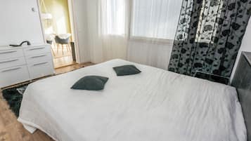 Un dormitorio con cama, dos almohadas, cómoda y ventana con cortinas.