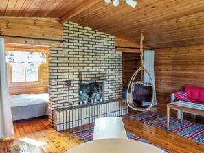 A cozy room with a brick fireplace, wooden ceiling, a hanging chair, and a bed. - Villa kaivopuisto by Interhome (Lavia)