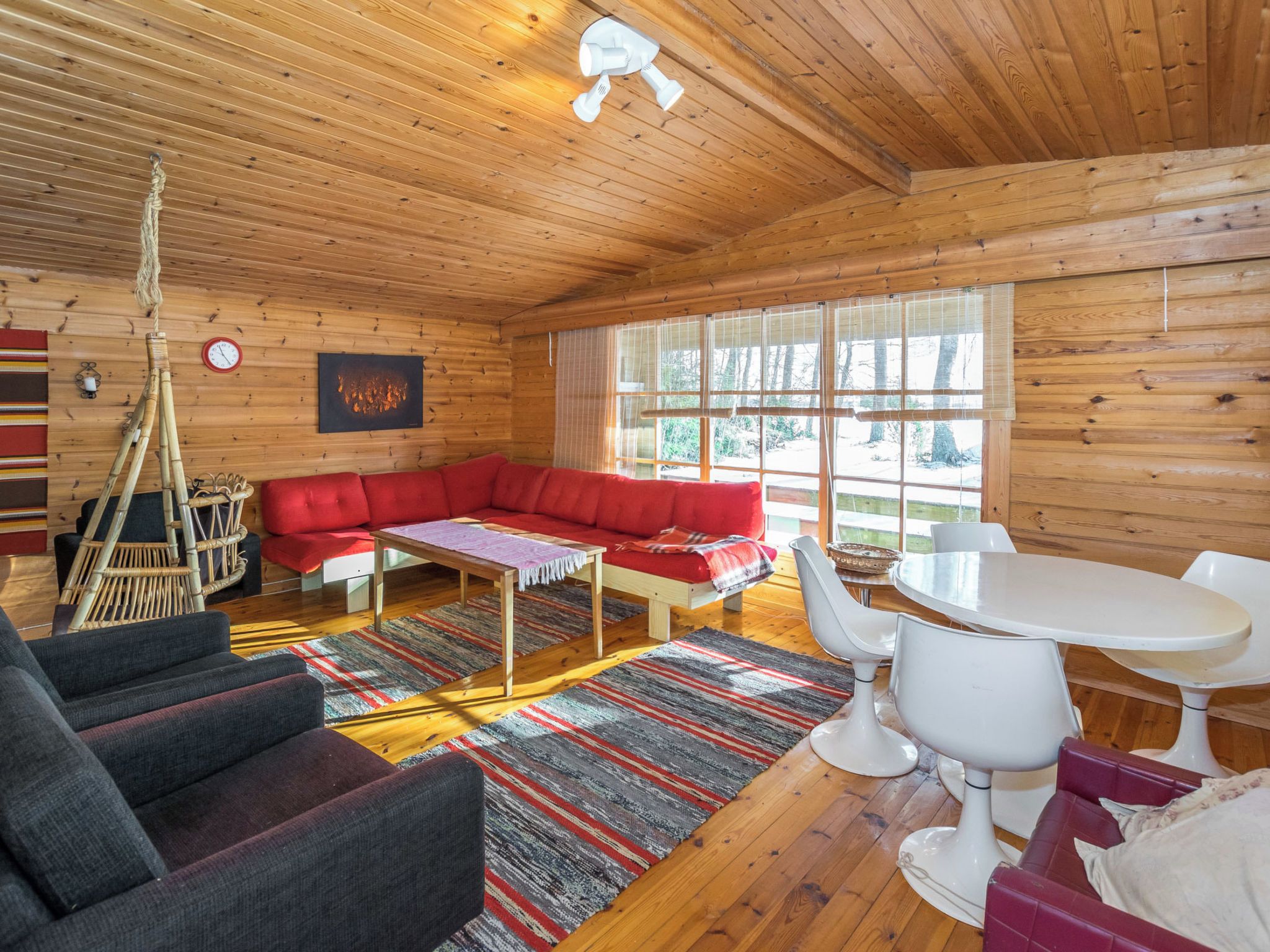 Interior de uma cabana de madeira com um sofá vermelho, uma mesa de jantar e um lustre.