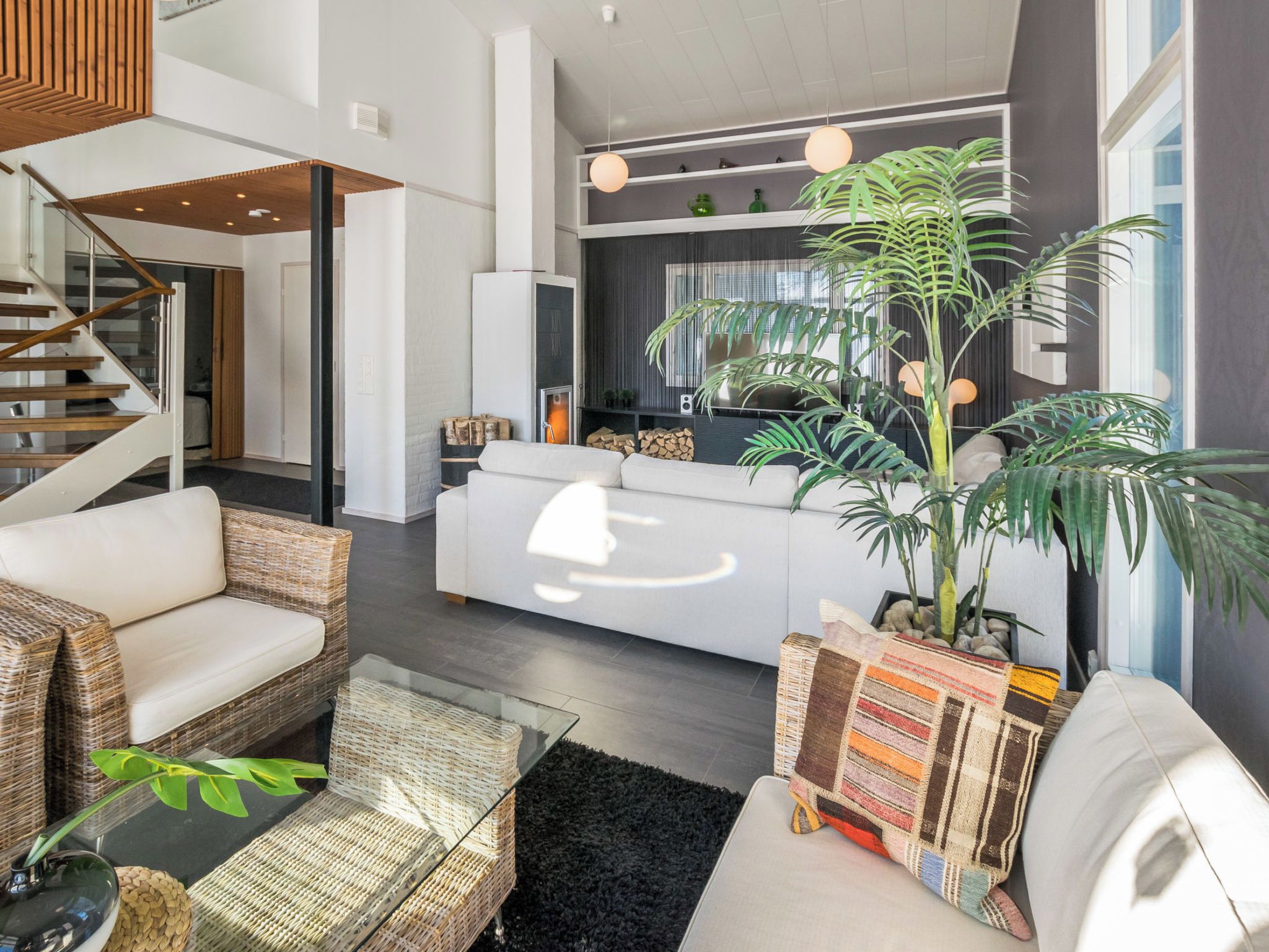 Un salon moderne avec un canapé, des fauteuils en osier, une table basse et une grande plante en pot.