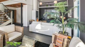 Un salon moderne avec un canapé, des fauteuils en osier, une table basse et une grande plante en pot.