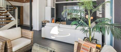 Una sala de estar moderna con un sofá, sillas de mimbre, una mesa de centro y una planta grande en maceta.