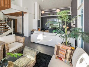 Un salon moderne avec un canapé, des fauteuils en osier, une table basse et une grande plante en pot.