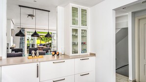 A modern kitchen with white cabinetry, black pendant lights, and a marble backsplash.
