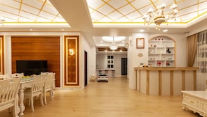 A spacious living room with a wooden dining table, white chairs, a TV, and a chandelier. - Honeysuckle Family Castle (Wujie)