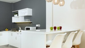 A modern kitchen with white cabinetry, a central island, and a dining area with white chairs. - Plaka Heart (Athens)