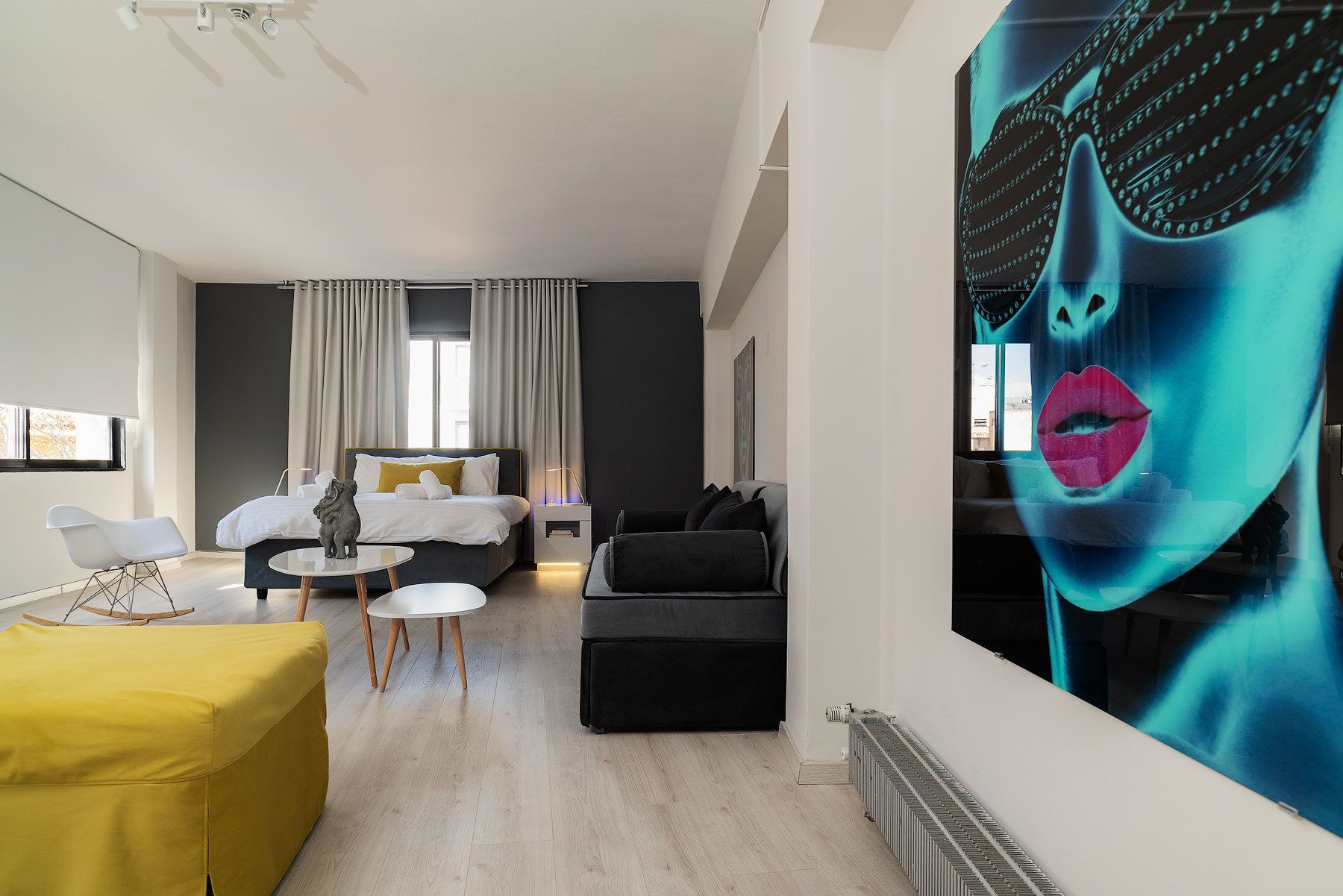 A modern hotel room with a bed, a sofa, a small table, and a large painting on the wall.
