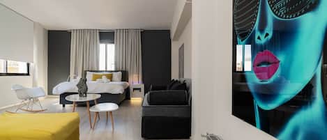 A modern hotel room with a bed, a sofa, a small table, and a large painting on the wall.