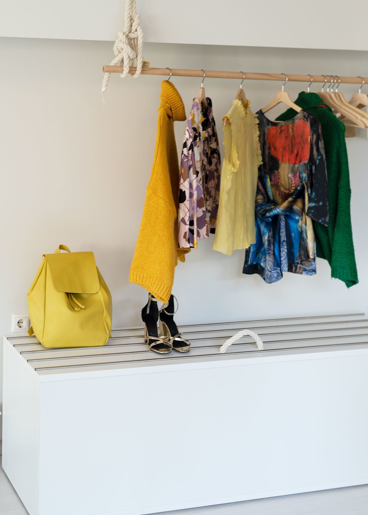 A white shelf with a hanging clothes rack above it, displaying various garments and a yellow bag.