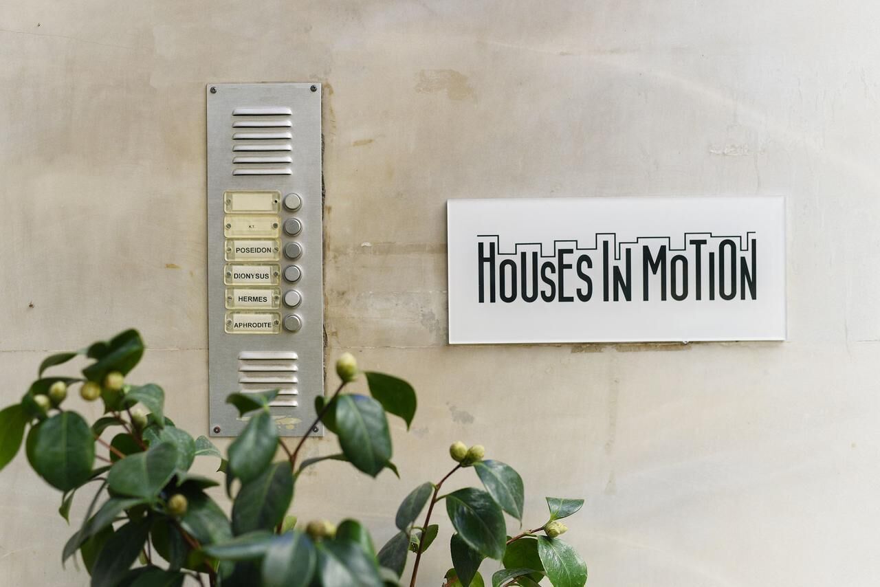A wall-mounted panel with buttons labeled "POSEIDON," "DIONYSUS," "HERMES," and "APHRODITE," and a sign reading "Houses in Motion."