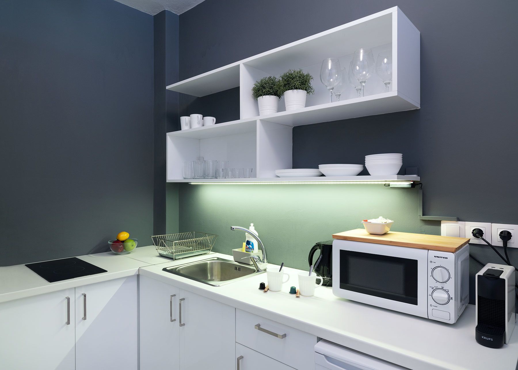 Une cuisine moderne avec des meubles blancs, un four à micro-ondes encastré, une bouilloire et un égouttoir à vaisselle.