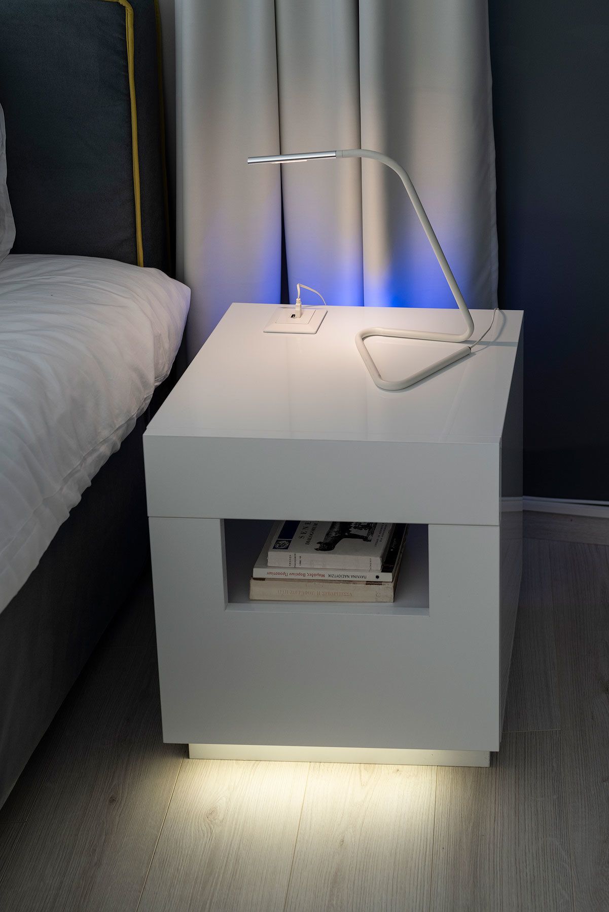A modern bedside table with a built-in lamp and a shelf for books.