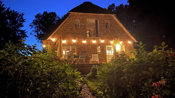 A brick house with a porch, string lights, and a garden path leading to the entrance. - Stylish under thatch with park-like garden on the island Eiderstedt / Oldenswort (Oldenswort)