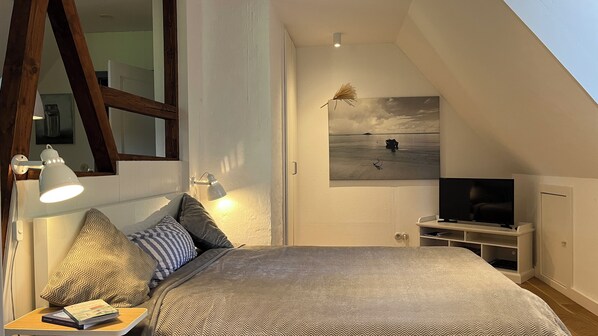 Ein Schlafzimmer mit einem großen Bett, einem Fernseher, einem Schreibtisch mit Lampe und einem Meeresblick-Gemälde.