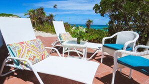 A patio with white wicker furniture, colorful cushions, and a small table with a vase of flowers. - Coral Beachside - Private Beach Resort (Greenwood)