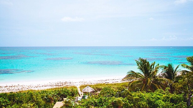 A beach with clear turquoise water, a sandy shore, and lush greenery. - Coral Beachside - Private Beach Resort (Greenwood)