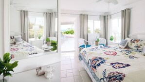 A hotel room with a large bed, a ceiling fan, a balcony with chairs, and a view of the outdoors. - Coral Beachside - Private Beach Resort (Greenwood)