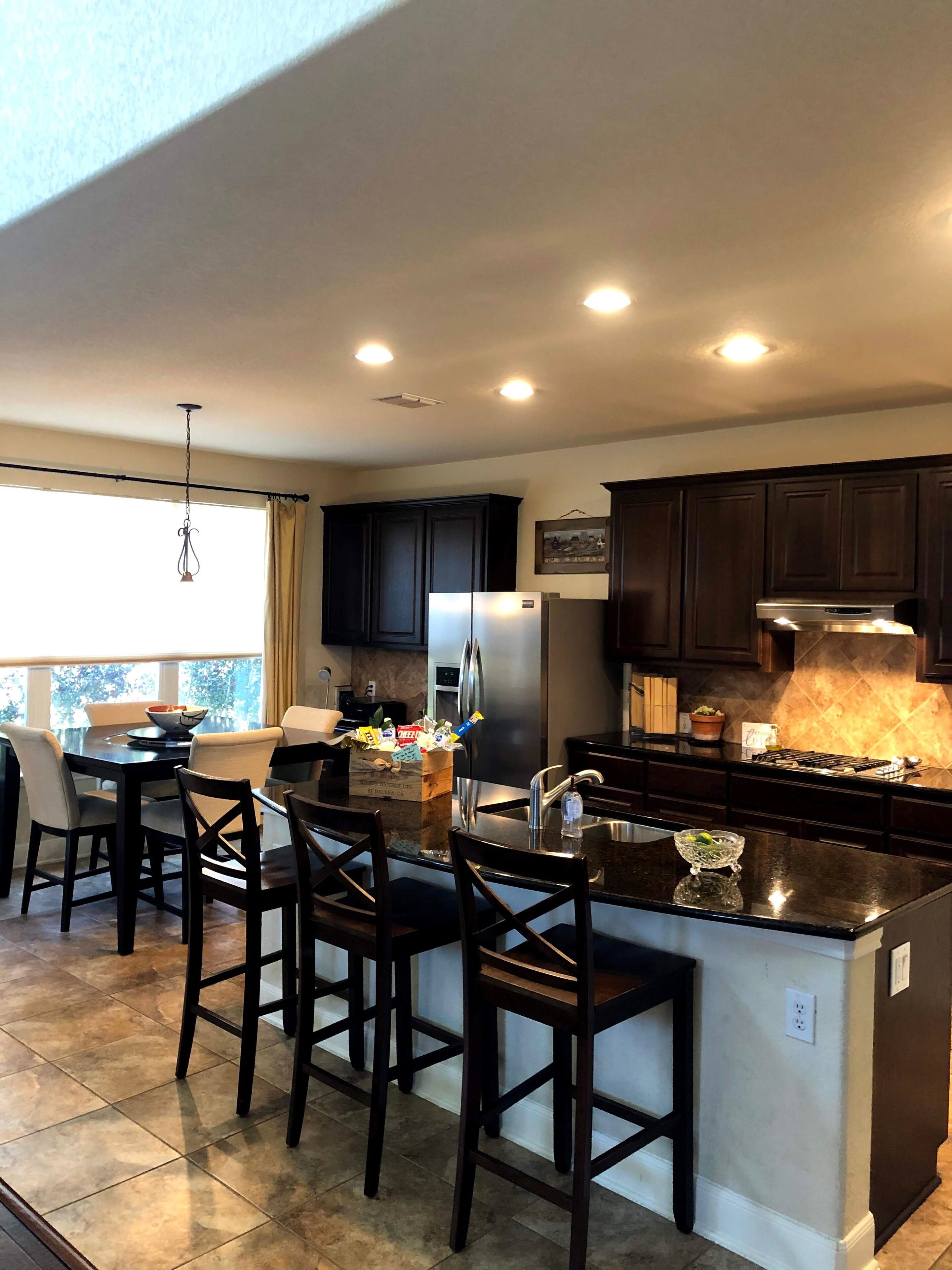 A modern kitchen with dark cabinetry, a central island with bar stools, a refrigerator, and a stove.