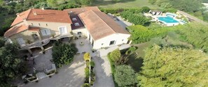 A large house with a swimming pool, surrounded by greenery and a driveway.