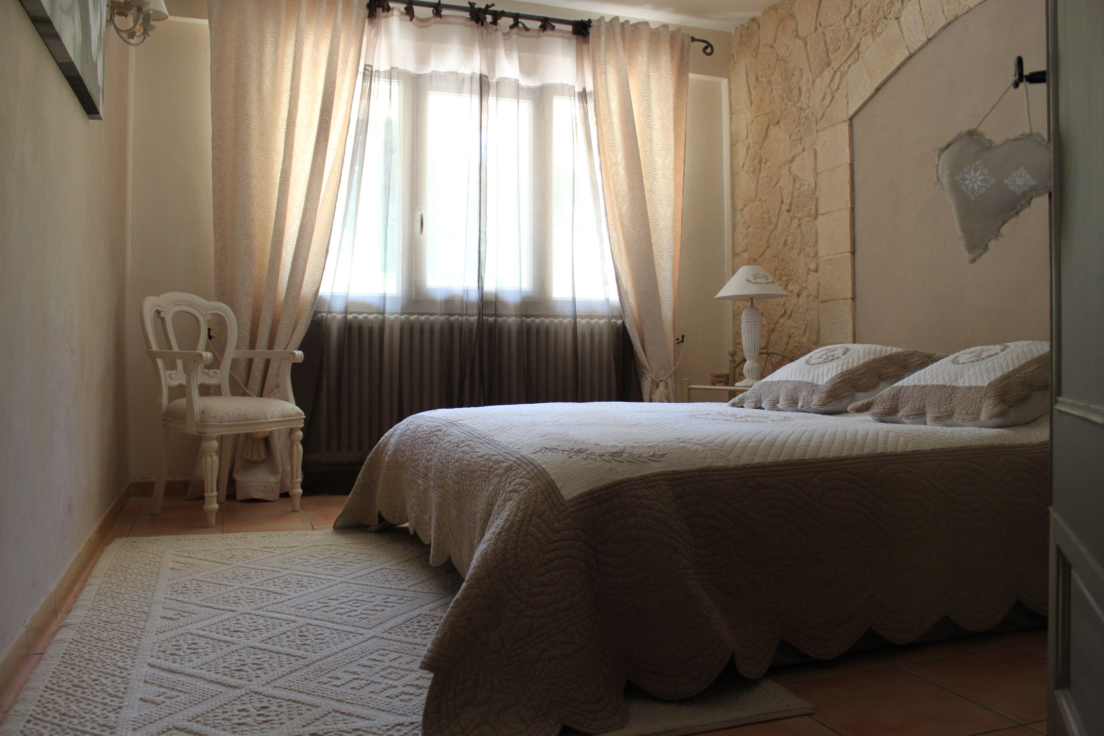 A bedroom with a bed, a chair, a lamp, and a window with curtains.
