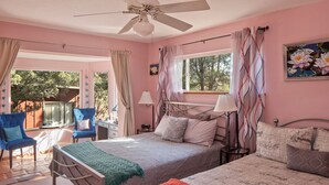 Une chambre avec deux lits, un ventilateur de plafond, une fenêtre avec des rideaux, un bureau avec une lampe et une chaise.
