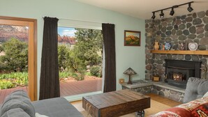 Un salon avec une cheminée en pierre, un canapé, une table basse et une vue sur un jardin et des montagnes.