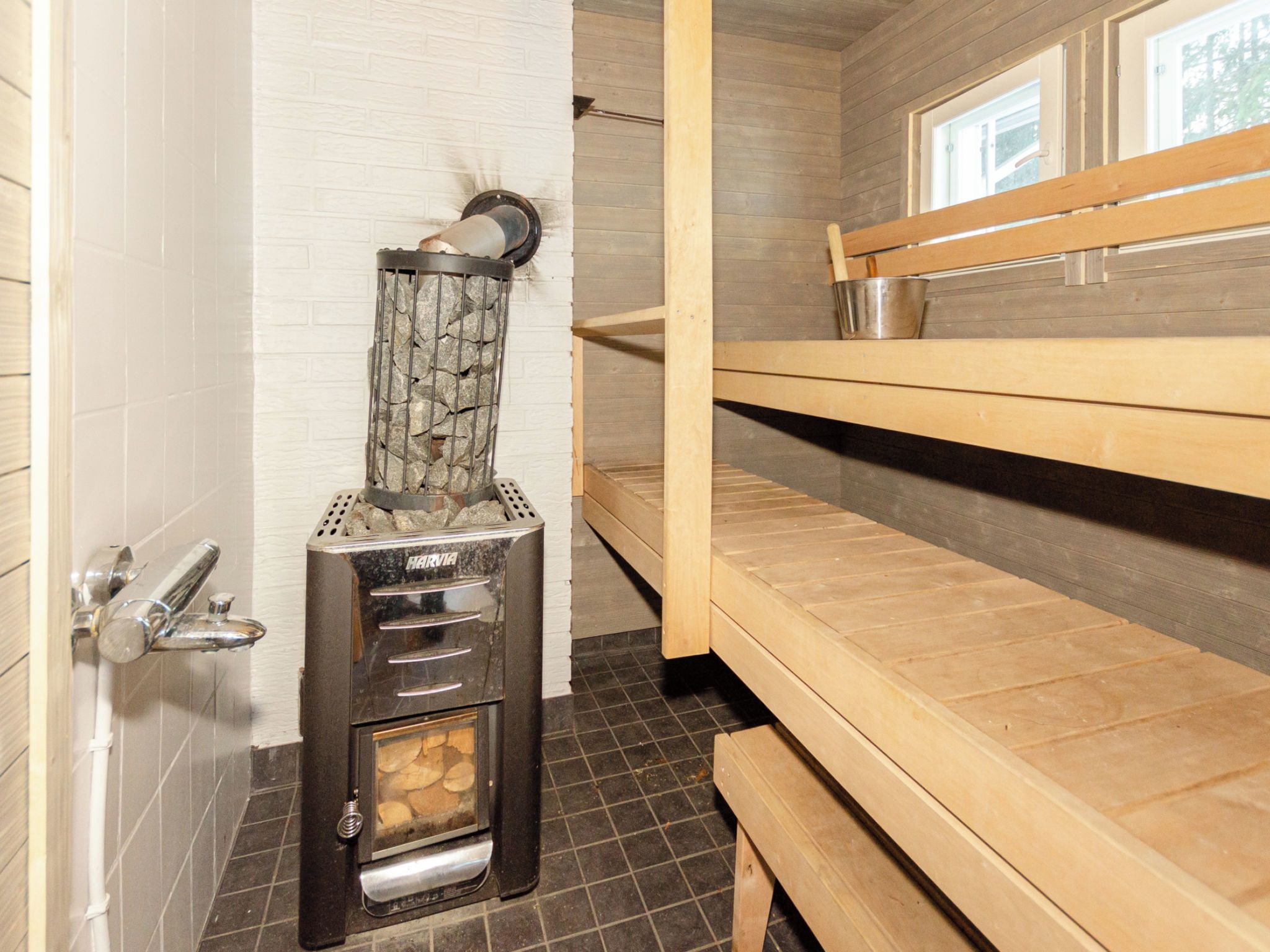 A bathroom with a Harvia sauna, a wooden bench, and a metal bucket on the shelf.