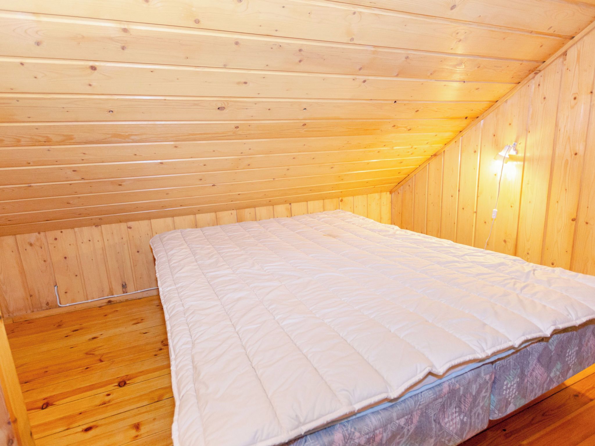 A small, single-bed room with wooden walls and a sloped ceiling.