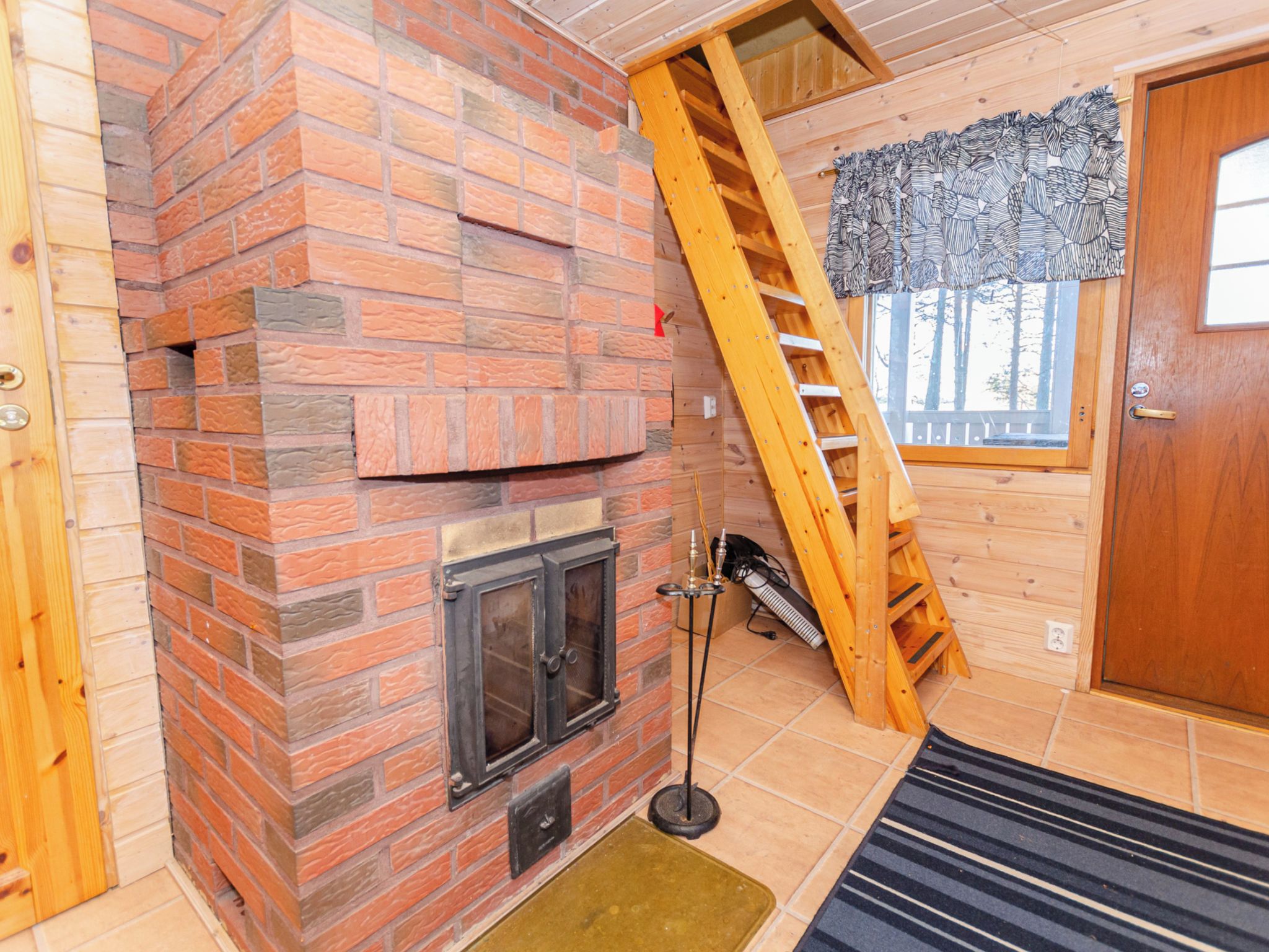 Ein Zimmer mit einem Kamin aus Ziegelsteinen, einer Holzleiter und einer Tür mit einem gemusterten Vorhang.