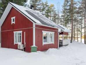 A red wooden cabin with a snow-covered roof, a porch, and a small attached shed. - Koivupirtti by Interhome (Juuka)
