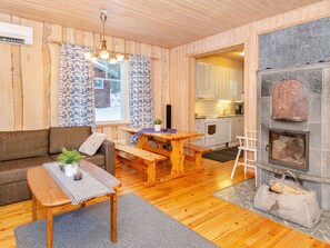 A cozy interior with a wooden floor, a sofa, a dining table, and a kitchen area with a stone fireplace. - Koivupirtti by Interhome (Juuka)