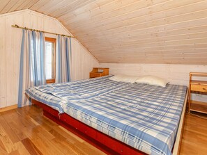 A bedroom with a wooden ceiling, a bed with a plaid bedspread, a nightstand, and a window with curtains. - Koivupirtti by Interhome (Juuka)