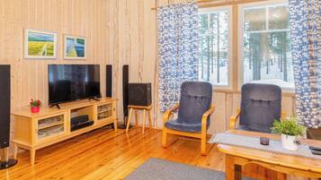 Ein gemütliches Zimmer mit Holzwänden, einem Fernseher, zwei Stühlen, einem Tisch und einem Fenster mit Vorhängen.