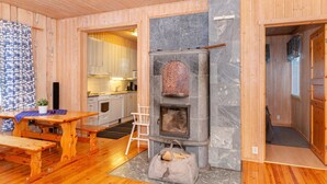 A cozy cabin interior with a stone fireplace, wooden floors, a dining table, and a kitchen area.